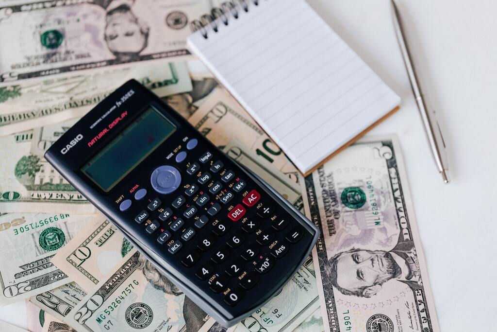 Calculator, notepad, and pen on top of some dollar bills.