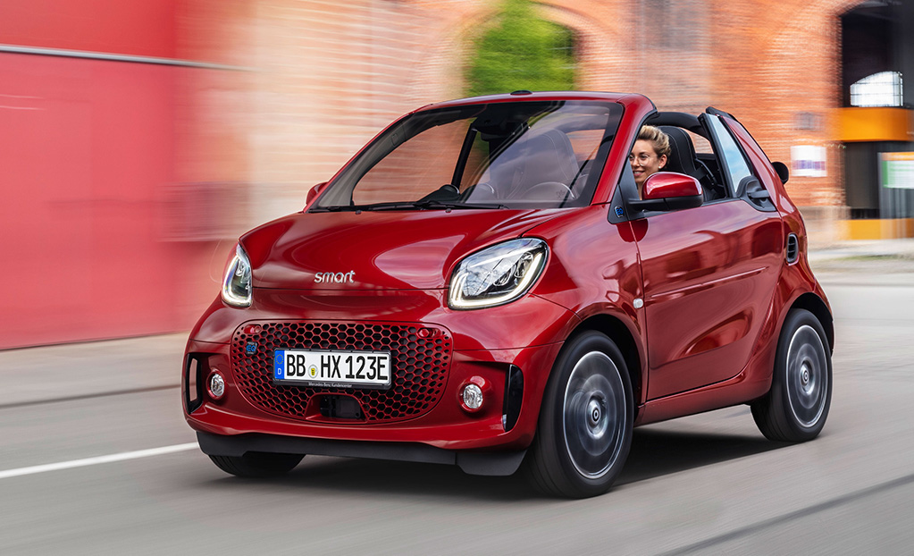Woman driving a red Smart EQ Fortwo Cabrio with the roof down.