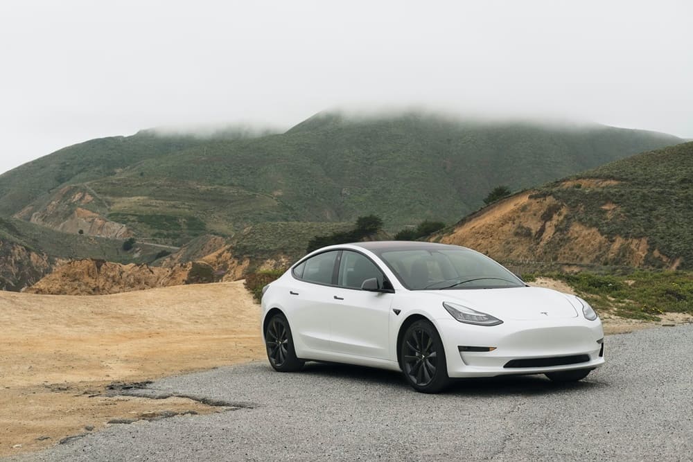A white Tesla Model 3 parked in front of a beautiful vista