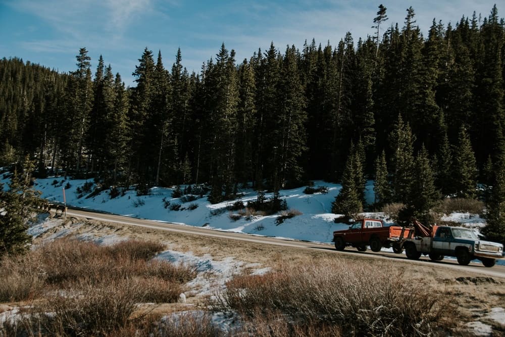 A tow truck towing a vehicle while passing by a forest