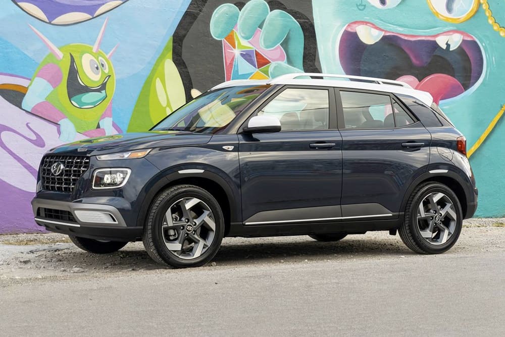 A parked black 2023 Hyundai Venue beside a graffiti wall