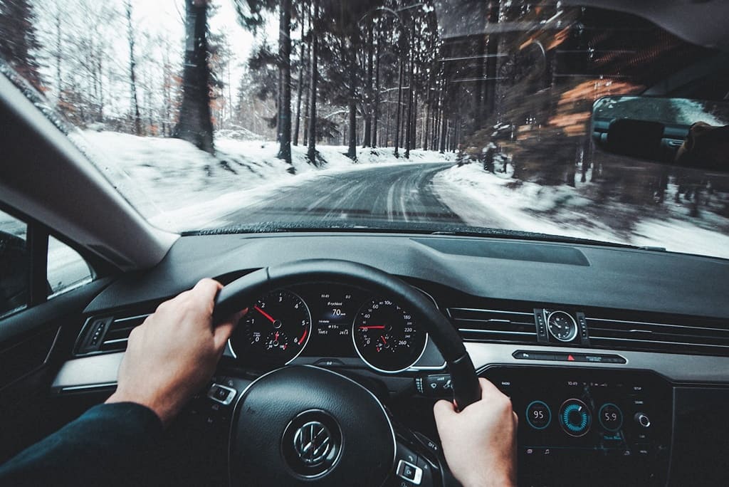 A person driving their car down a road past a snow-covered forest